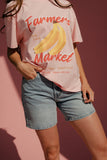 Person wearing a pink t-shirt with a banana graphic and 'Farmers Market' text on a pink background