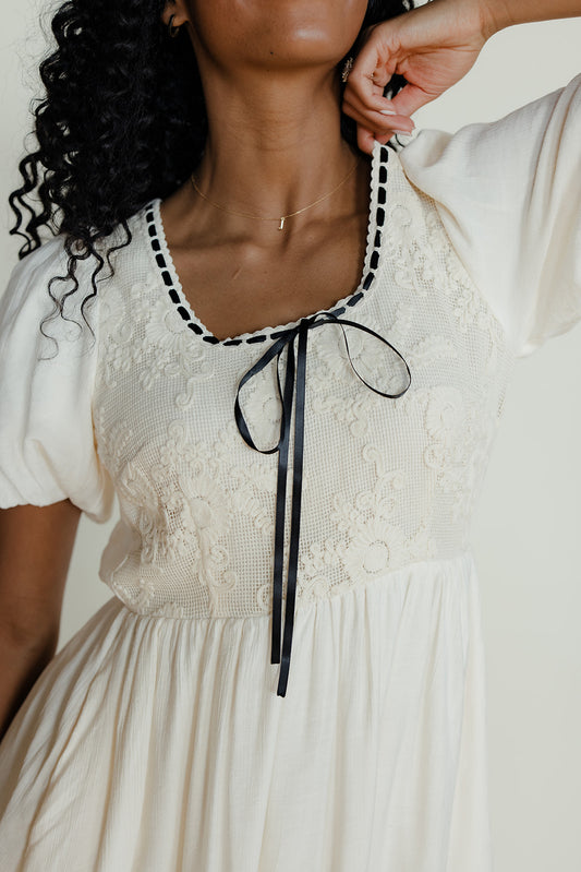 White dress with black trim and ribbon detail, worn by a person.