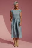 Woman wearing a light blue dress standing against a pink background