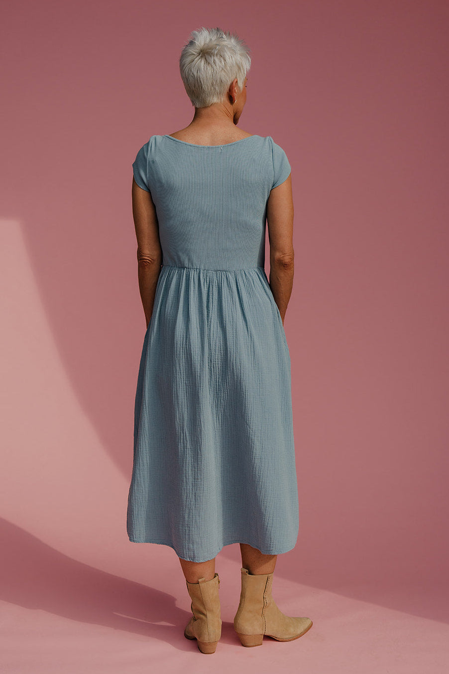 Person wearing a light blue dress standing against a pink background