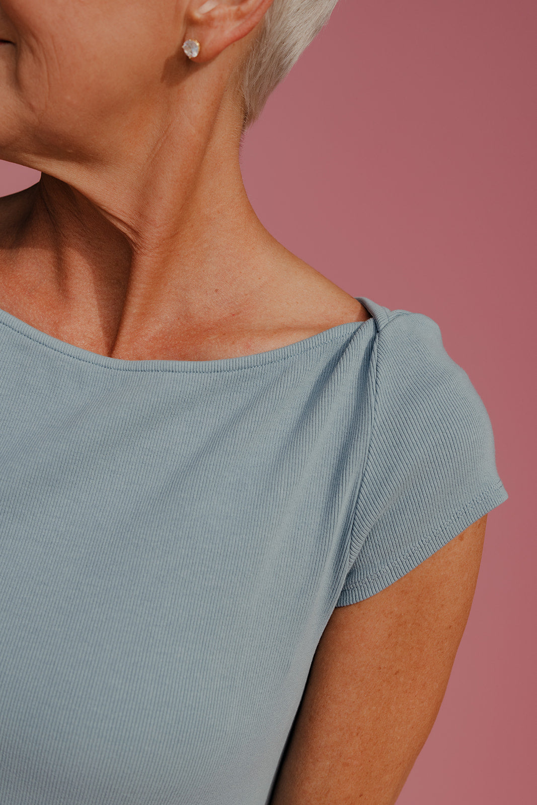 Close-up of a person wearing a light blue top against a pink background