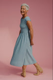 Woman in a light blue dress standing against a pink background