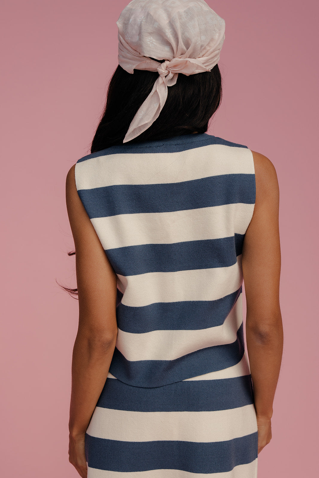 Person wearing a blue and white striped dress with a pink headscarf on a pink background