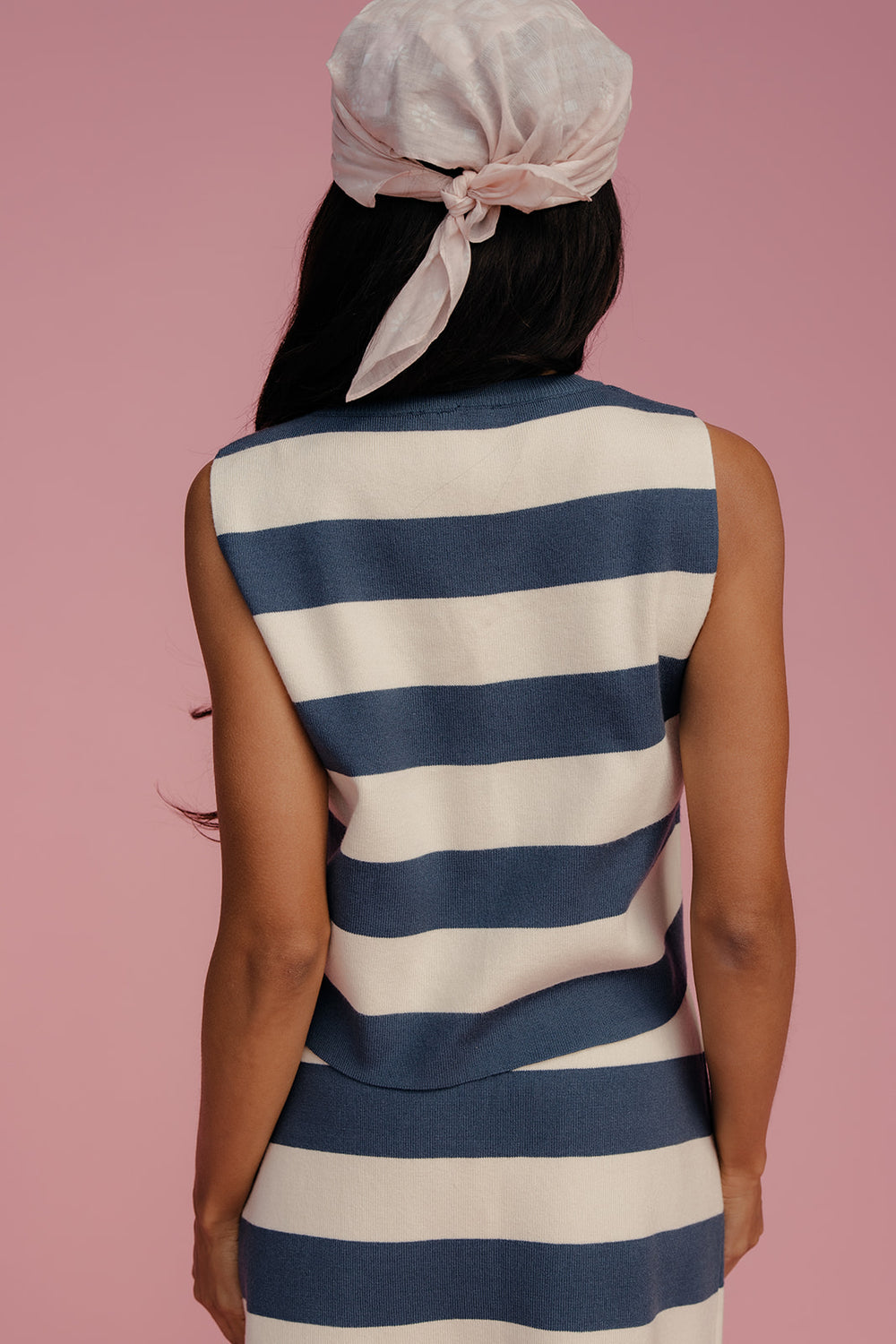 Person wearing a blue and white striped dress with a pink headscarf on a pink background