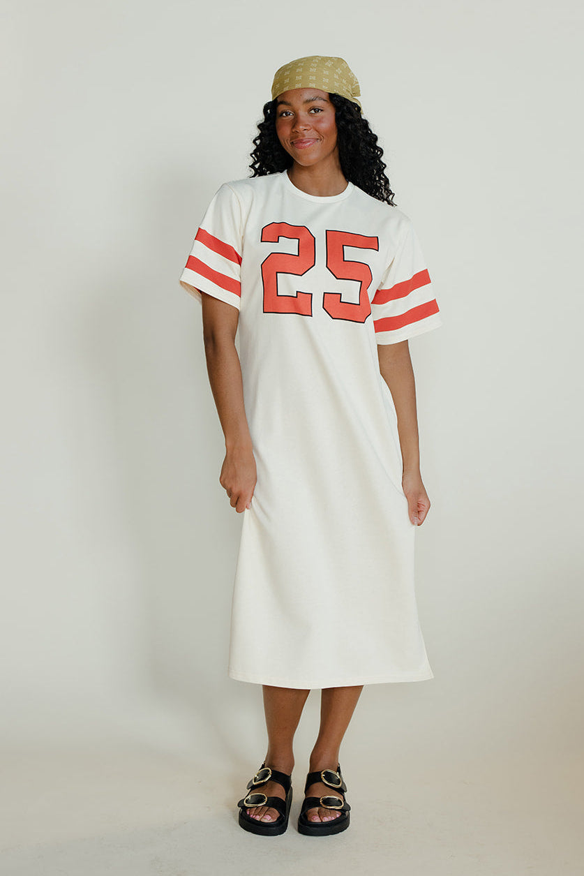 Woman wearing a white dress with red numbers standing against a plain background