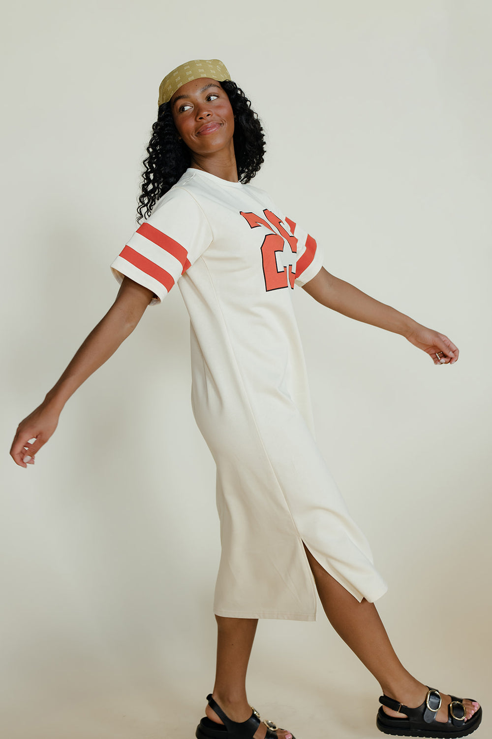 Woman wearing a white dress with red accents and a cap against a plain background