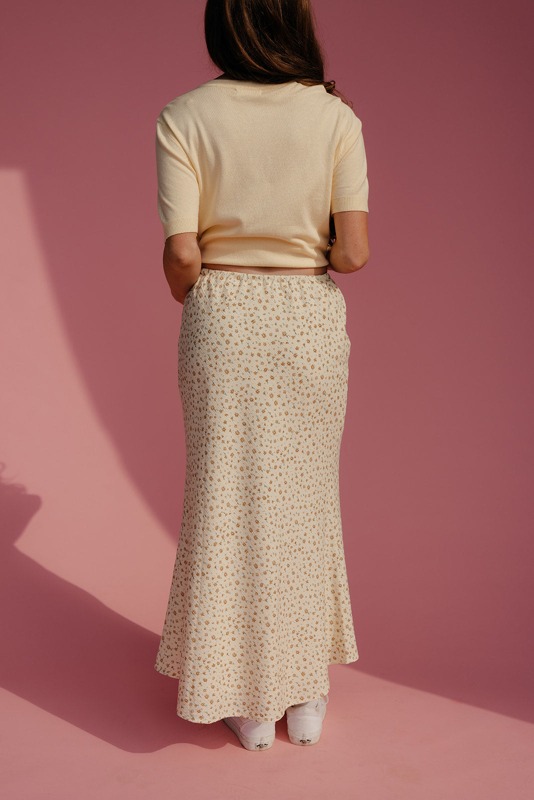 Person wearing a beige top and patterned skirt on a pink background