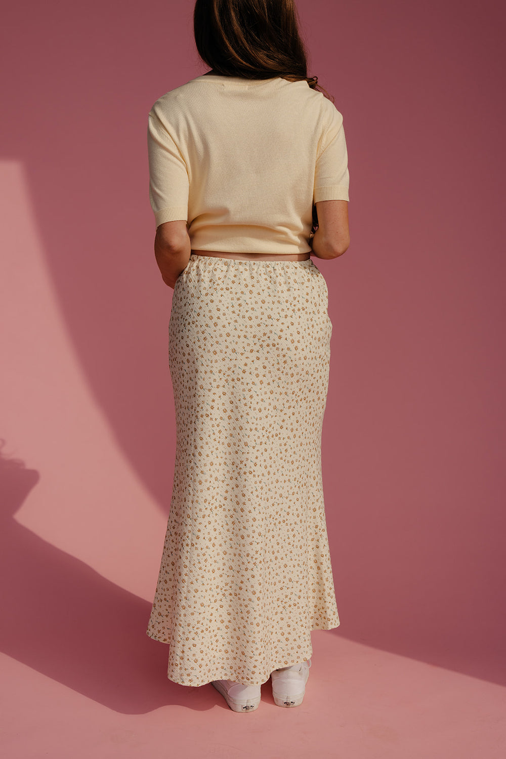 Person wearing a beige top and patterned skirt on a pink background