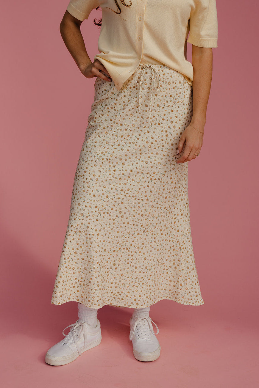 Person wearing a beige top and patterned skirt on a pink background