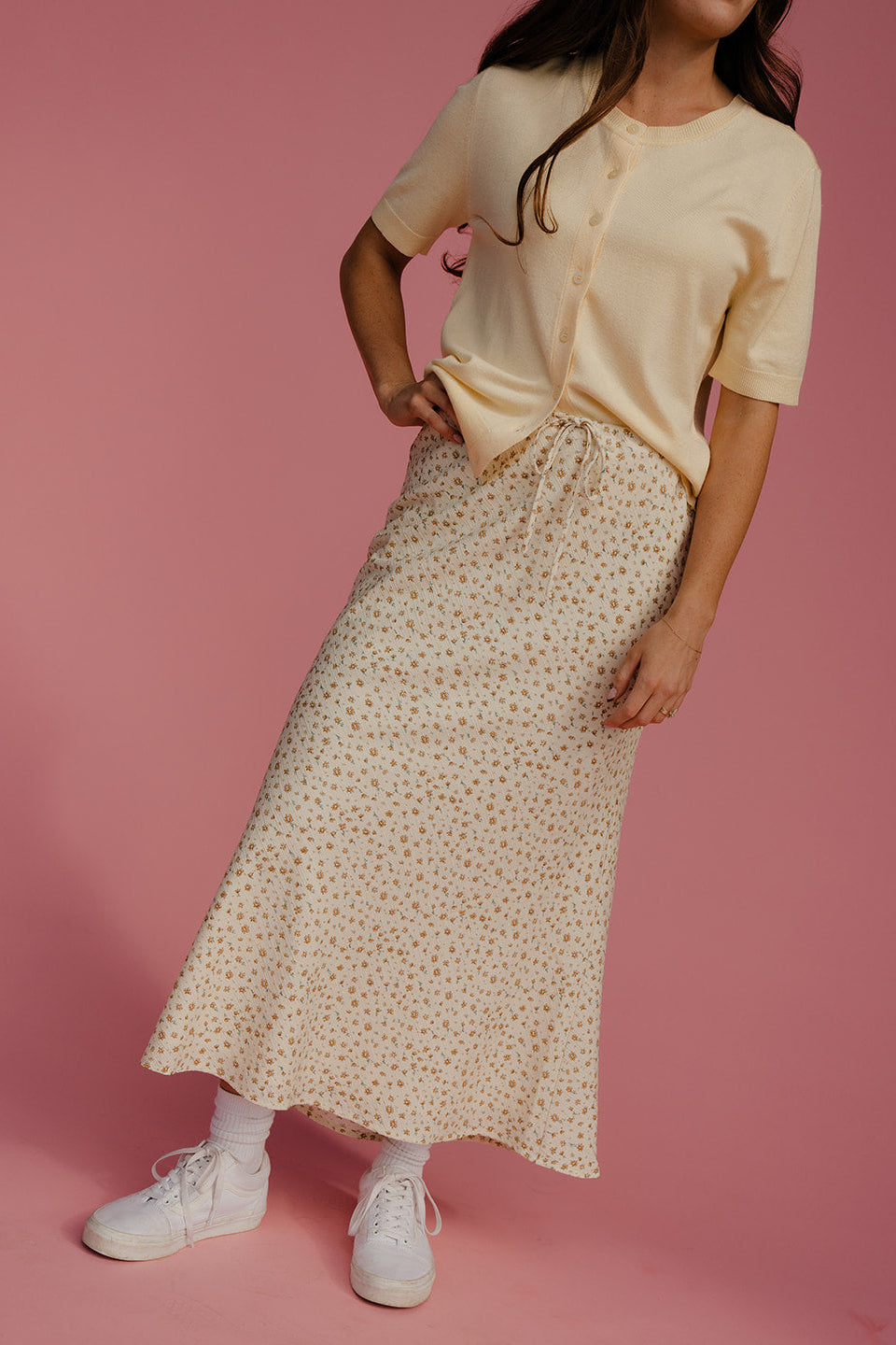 Woman wearing a beige top and patterned skirt on a pink background