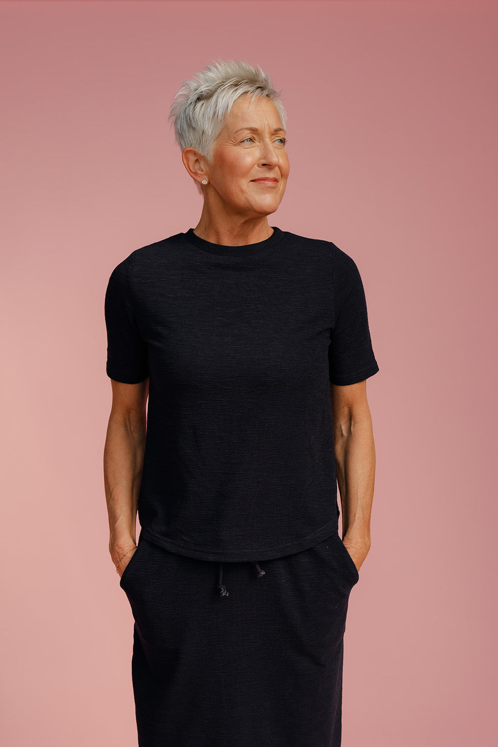 Person wearing a black outfit against a pink background