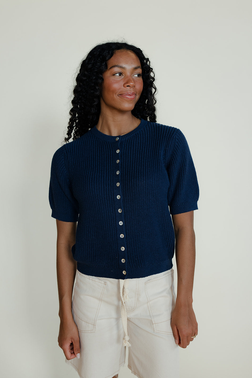 Woman wearing a navy blue short-sleeve cardigan with white buttons on a plain background