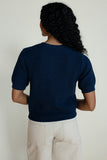 Person wearing a navy blue ribbed sweater and beige pants against a plain background