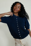 Woman wearing a navy blue ribbed sweater with buttons against a plain background