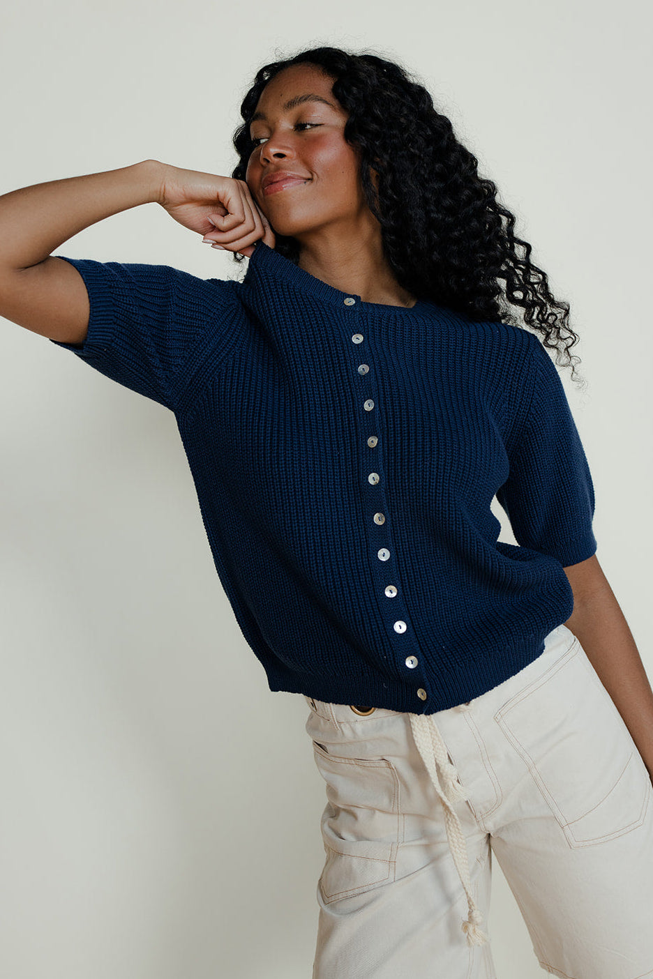 Woman wearing a navy blue cardigan with white buttons against a plain background