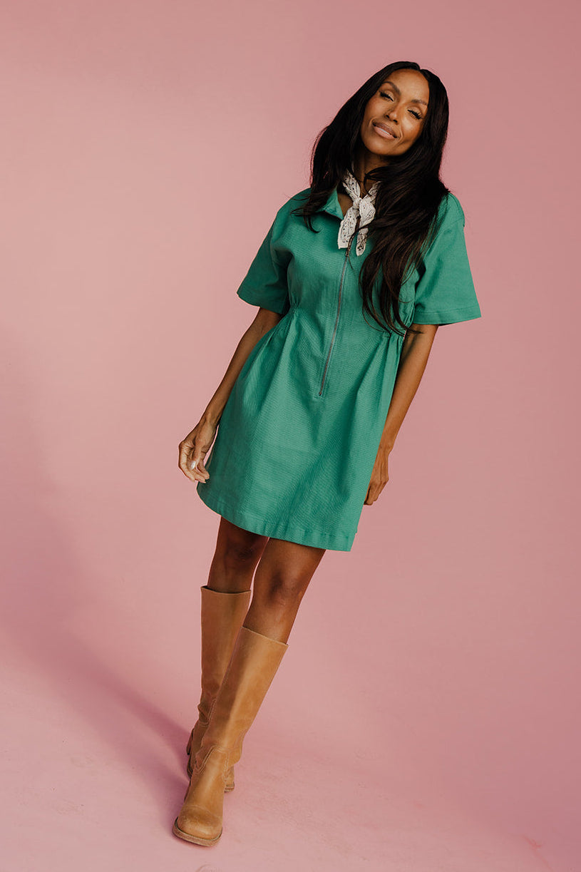 Woman wearing a green dress and brown boots on a pink background