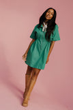 Woman wearing a green dress and brown boots on a pink background