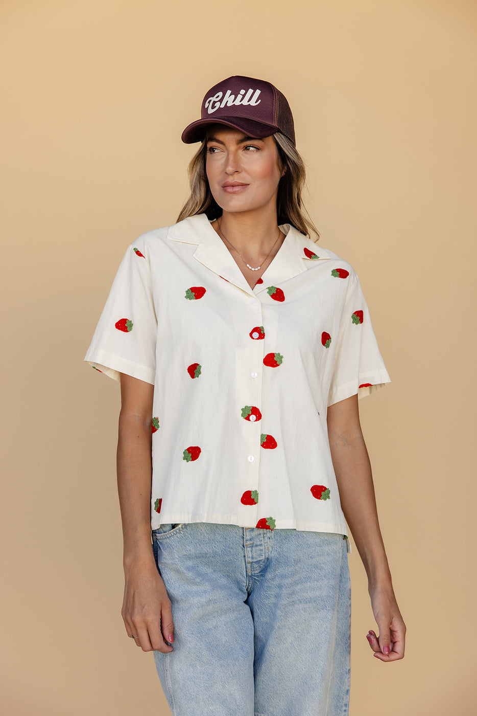 a woman wearing a hat and a white shirt with red and green fruits on it