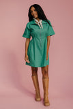 Woman wearing a green dress and brown boots on a pink background