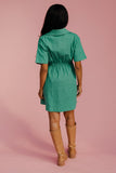 Person wearing a green dress and tan boots on a pink background