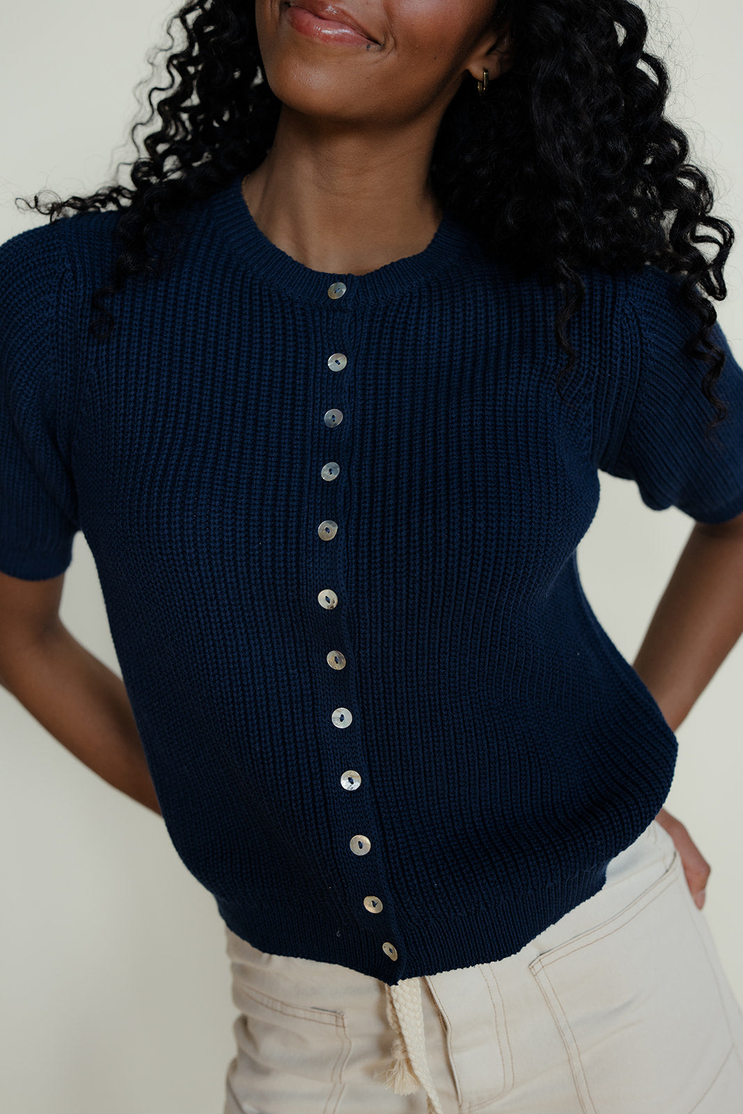 Woman wearing a navy blue ribbed sweater with silver buttons against a white background