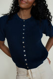 Woman wearing a navy blue ribbed sweater with silver buttons against a white background