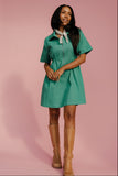 Woman wearing a green dress with a white collar and brown boots on a pink background