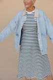Woman wearing a light blue denim jacket over a striped dress on a beige background
