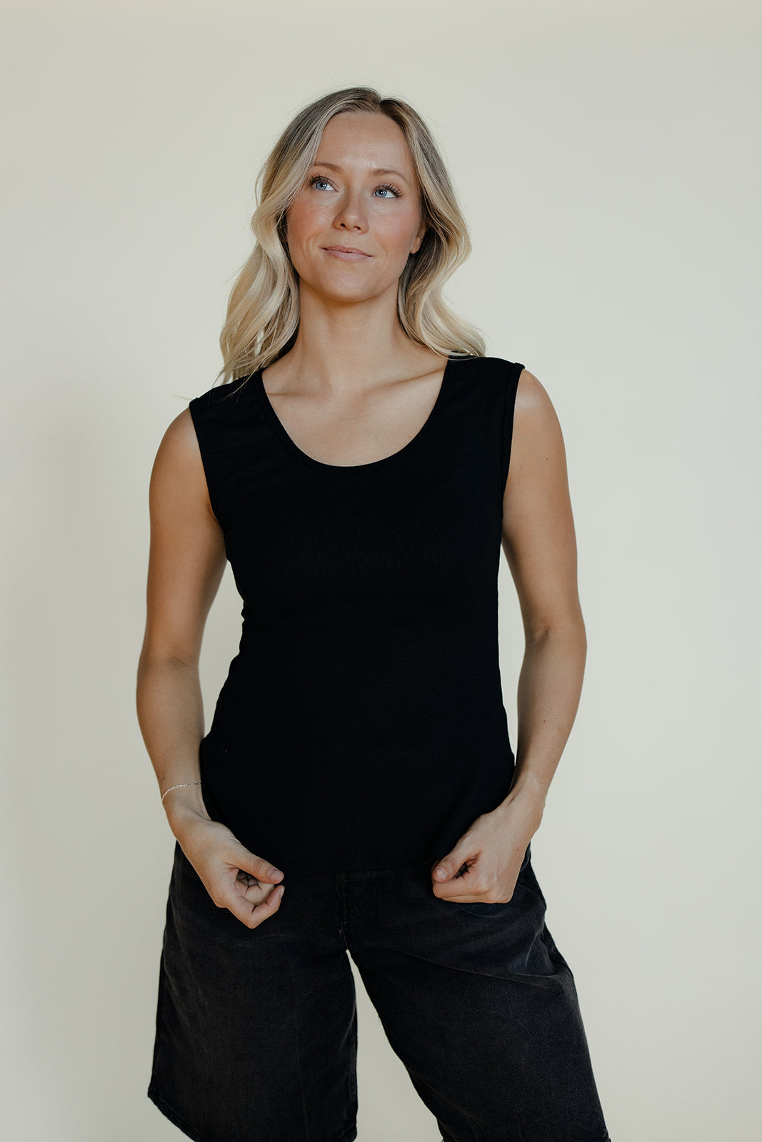 Woman wearing a black sleeveless top and black pants against a plain background