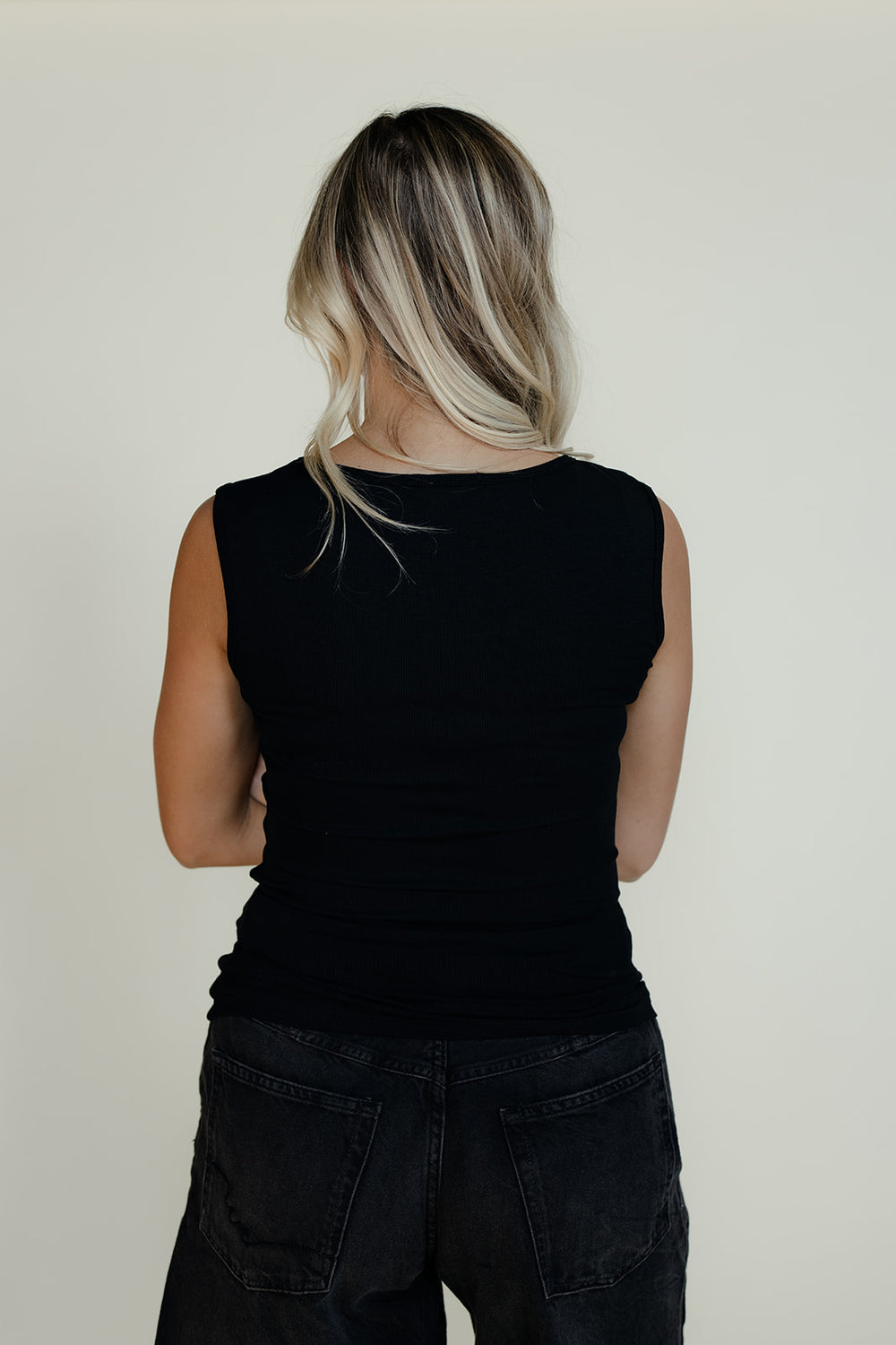 Person wearing a black sleeveless top and black pants against a plain background