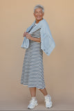 Woman wearing a striped dress and light jacket against a beige background