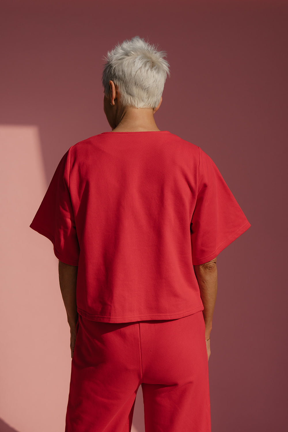 Person wearing a red outfit standing against a pink wall