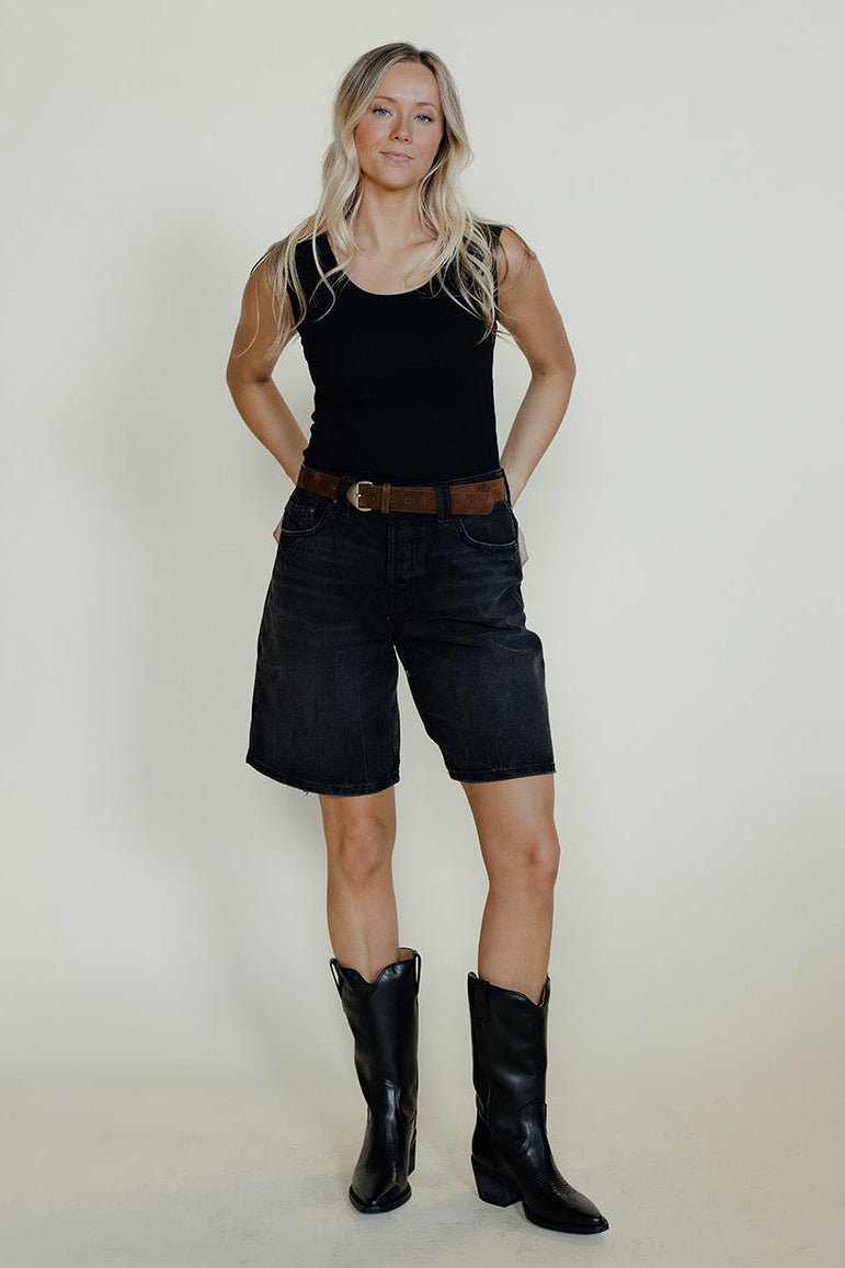 Person wearing a black sleeveless top, black shorts, and black boots on a plain background