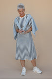 Woman wearing a black and white striped dress with a blue shawl against a beige background