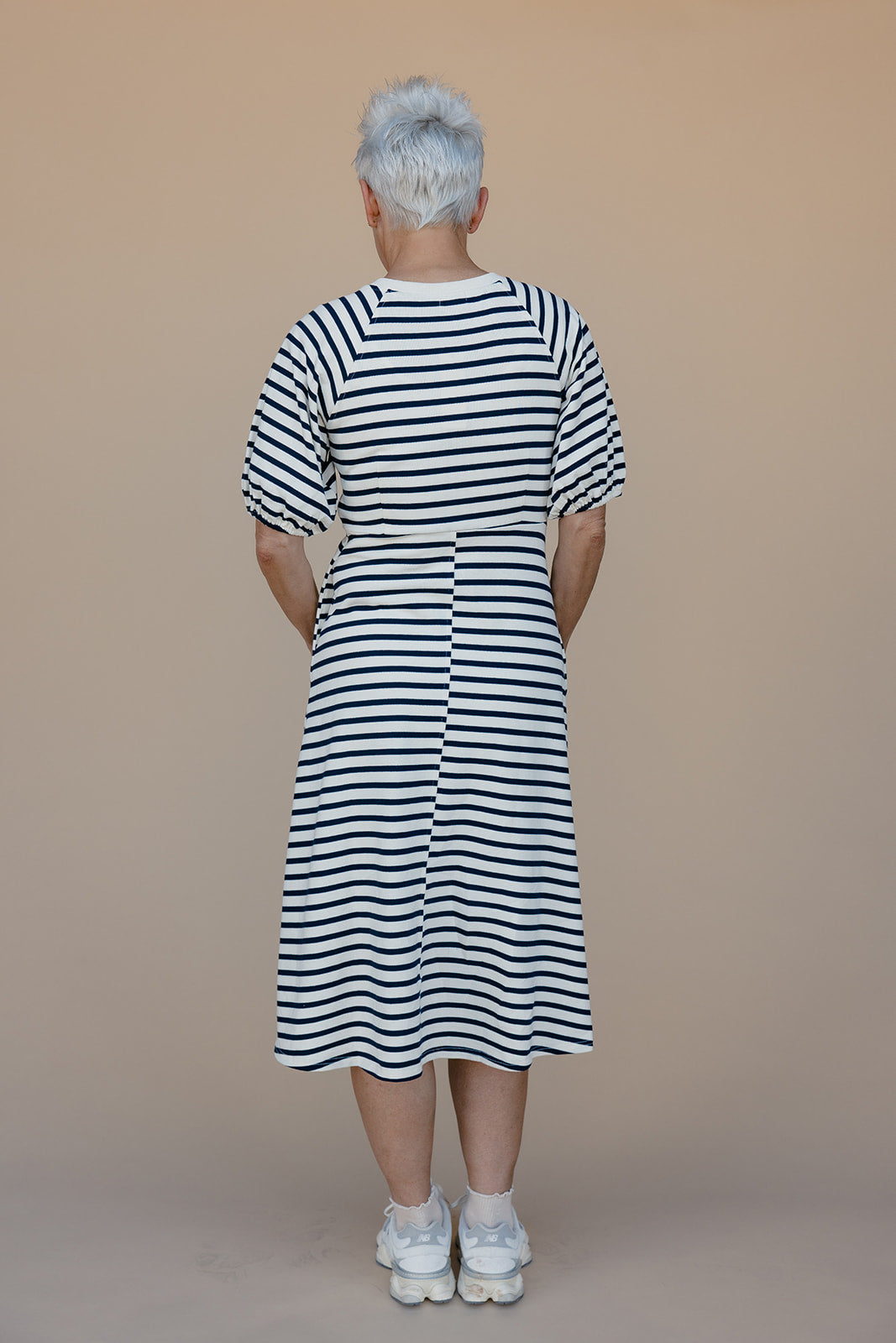 Person wearing a black and white striped dress against a beige background