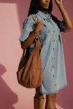 Woman wearing a denim dress holding a brown leather bag against a pink background