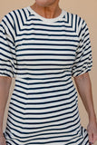Person wearing a white and navy striped dress against a beige background