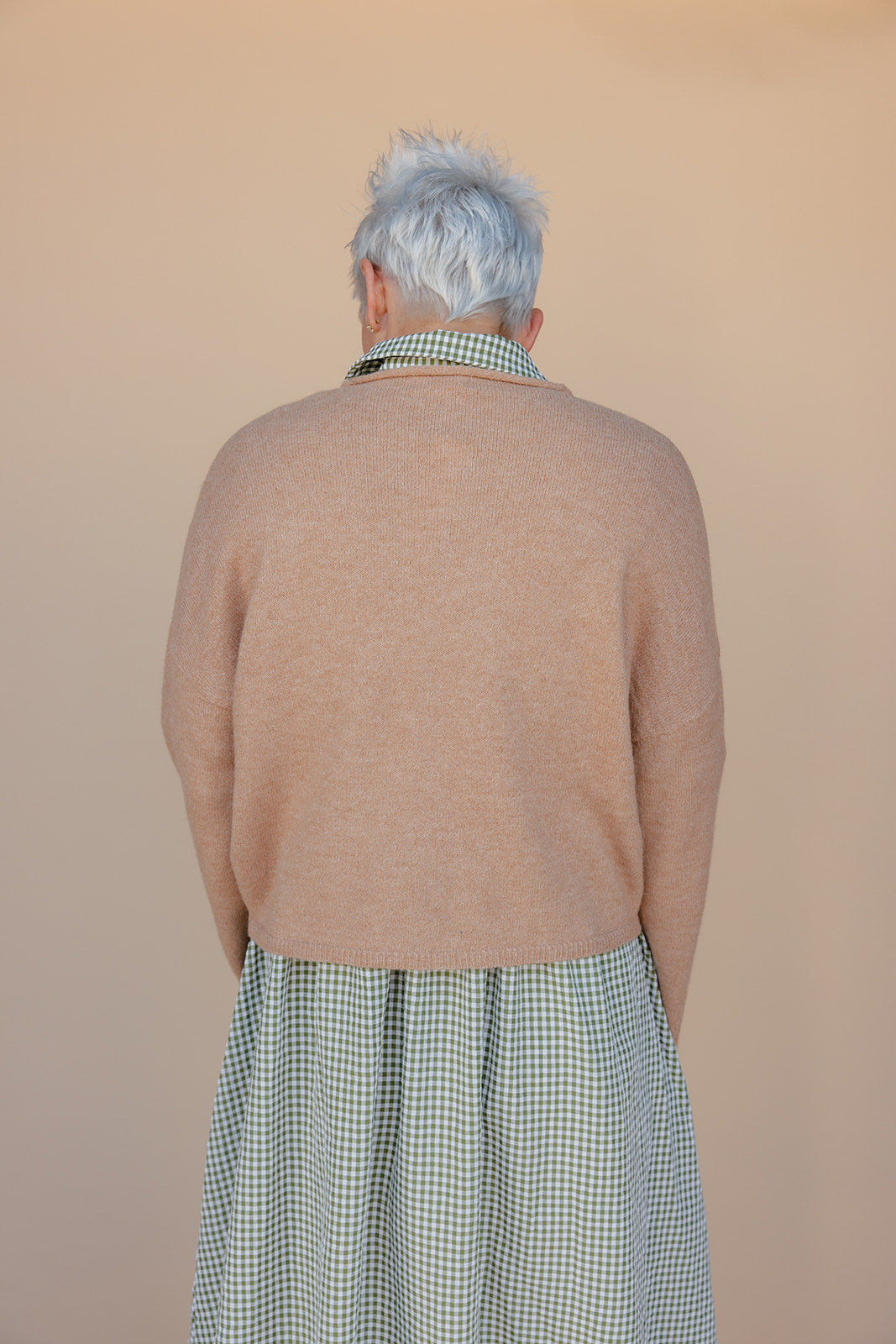 Person wearing a beige sweater and green checkered skirt against a beige background