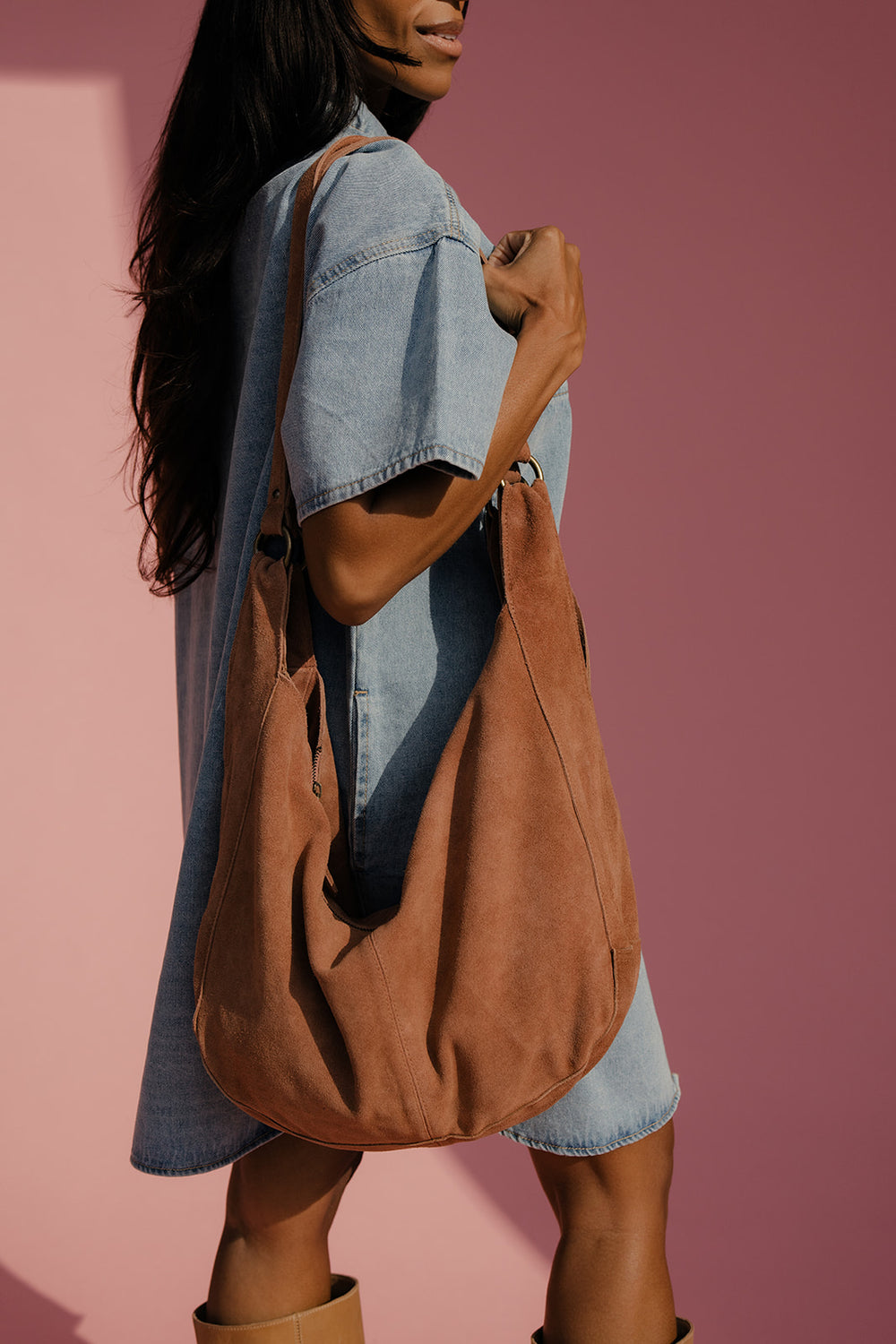 Woman holding a brown leather bag against a pink background