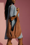 Woman holding a brown leather bag against a pink background
