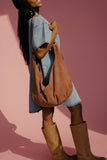 Woman holding a brown leather bag against a pink background