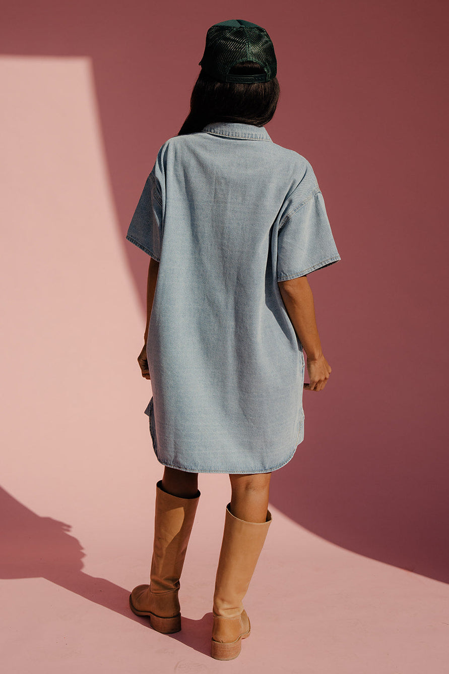 Person wearing a light blue dress and brown boots standing on a pink surface with a red background