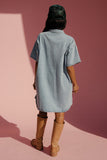 Person wearing a light blue dress and brown boots standing on a pink surface with a red background