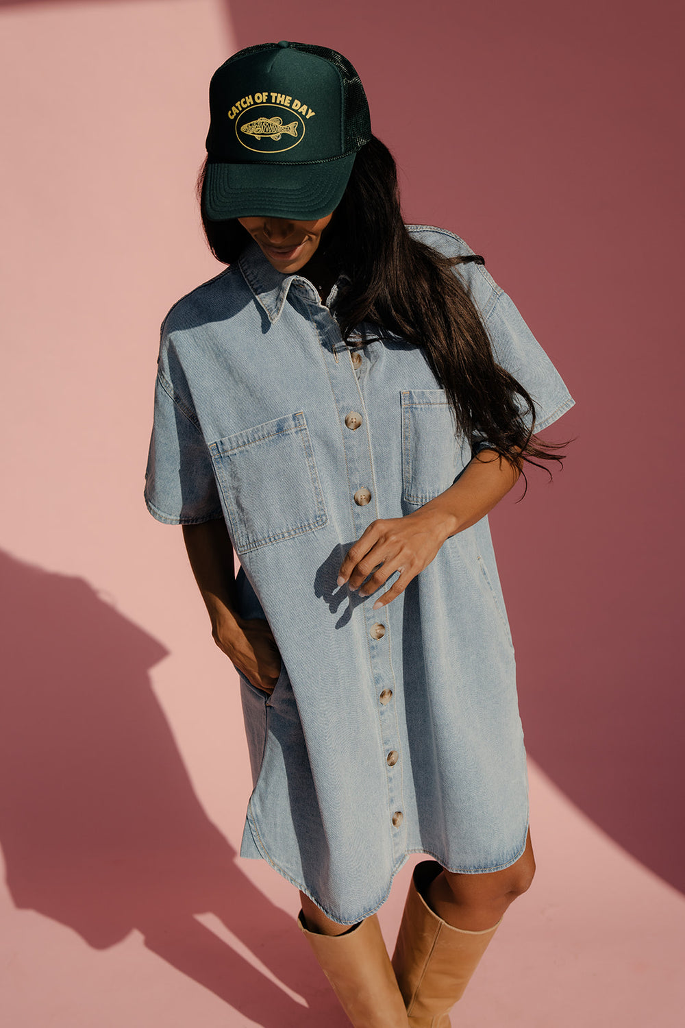 Woman wearing a denim dress and brown boots with a pink background