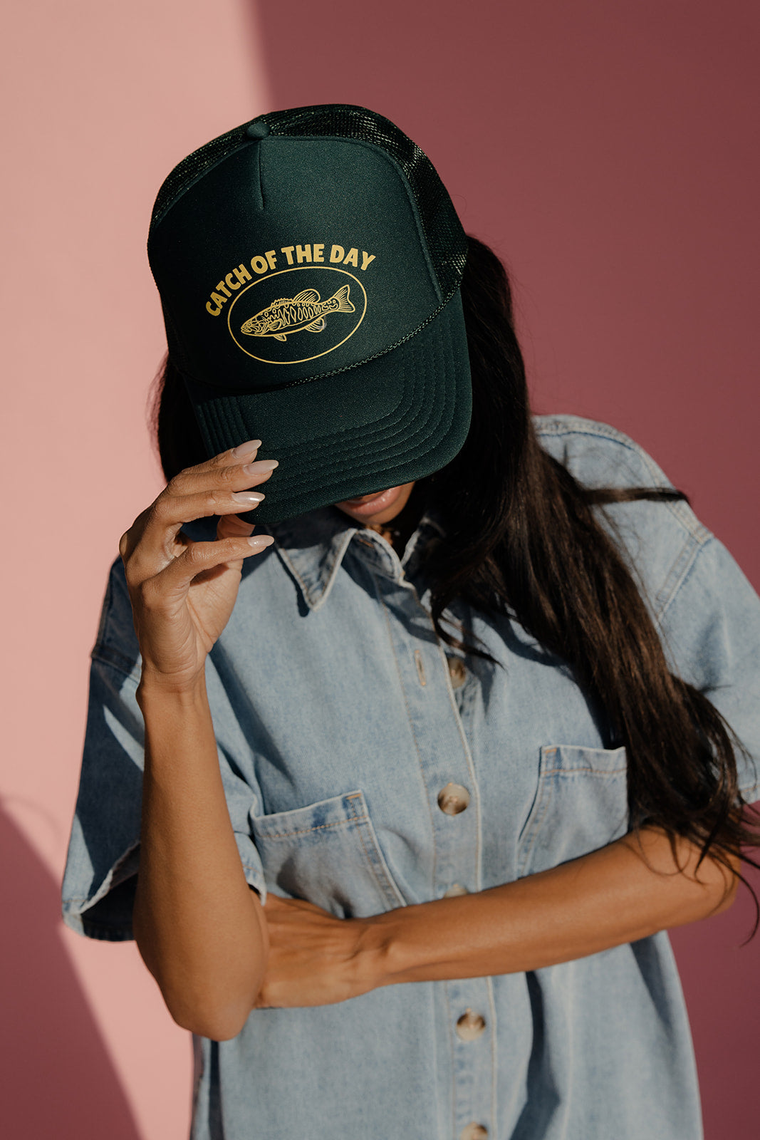 Person wearing a green cap with 'Catch of the Day' text against a pink background
