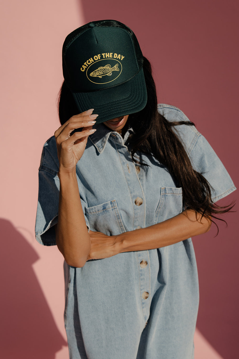 Person wearing a black cap with text and logo against a pink background
