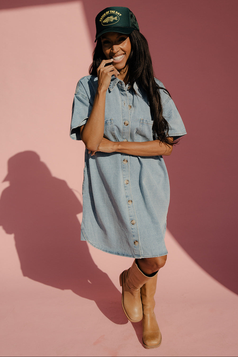 Woman wearing a denim dress and green cap against a pink background
