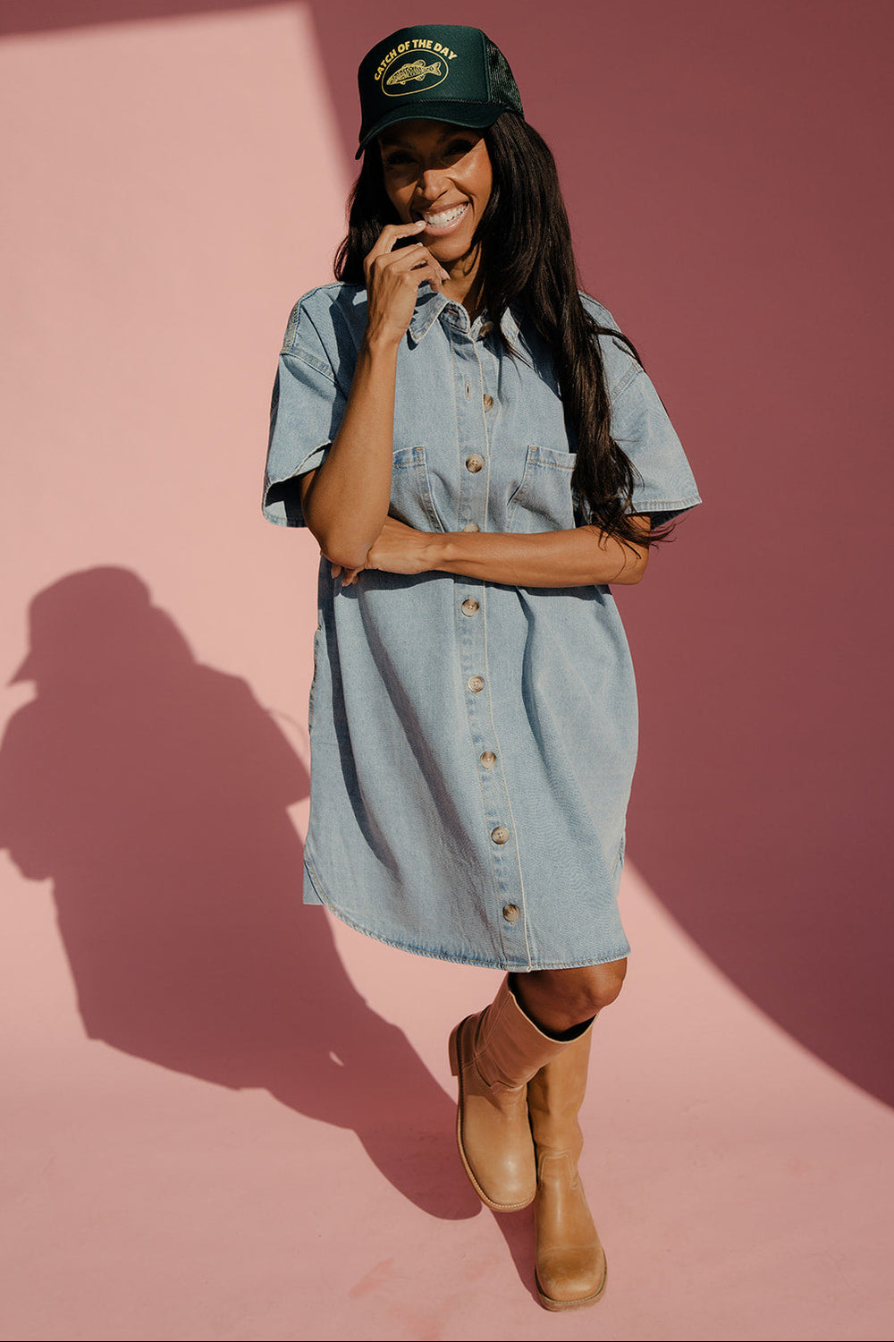 Woman wearing a denim dress and green cap against a pink background