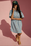 Woman wearing a denim dress and green cap against a pink background