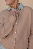 Close-up of a person wearing a brown cardigan with a checkered collar against a beige background
